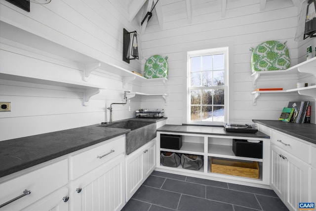 kitchen featuring sink, wood walls, white cabinets, and dark tile patterned flooring