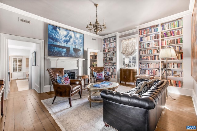 living area with crown molding, a notable chandelier, light hardwood / wood-style floors, and built in shelves