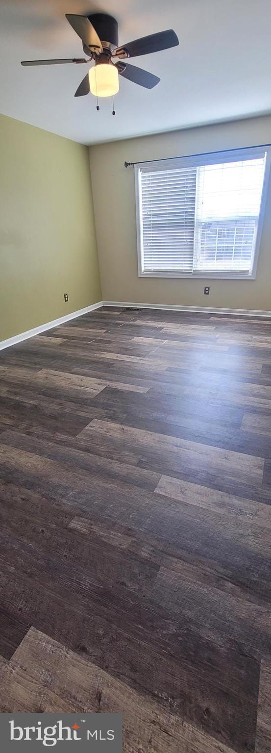 spare room with baseboards, dark wood finished floors, and a ceiling fan