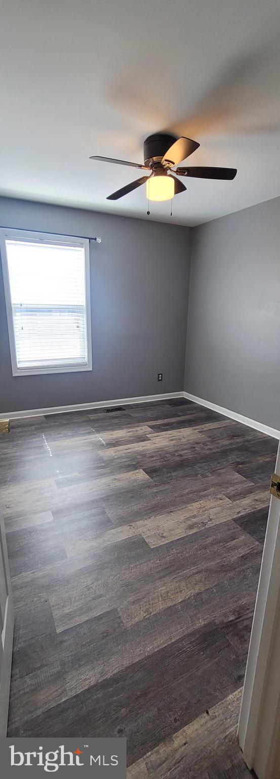 empty room featuring dark wood-type flooring, a ceiling fan, and baseboards