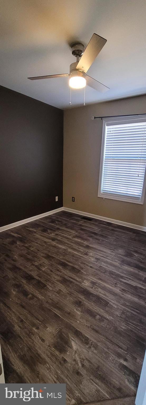 spare room with ceiling fan, baseboards, and dark wood-type flooring