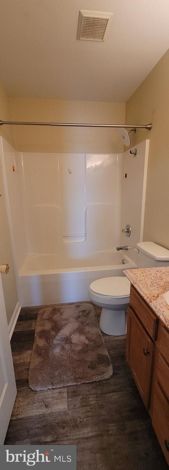 full bath with visible vents, toilet, washtub / shower combination, vanity, and wood finished floors