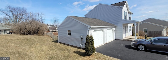 view of side of home with a garage, driveway, a lawn, and fence