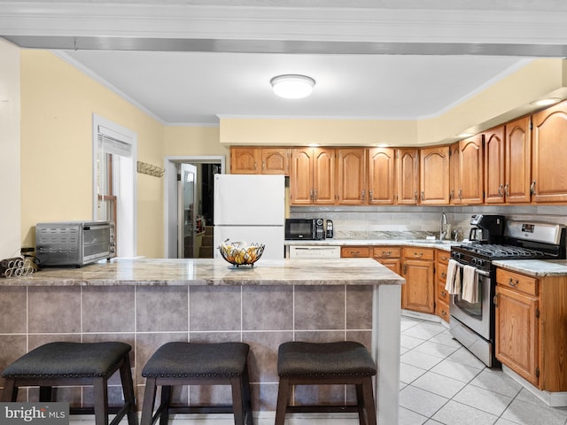 kitchen featuring a kitchen bar, light tile patterned floors, ornamental molding, kitchen peninsula, and white appliances