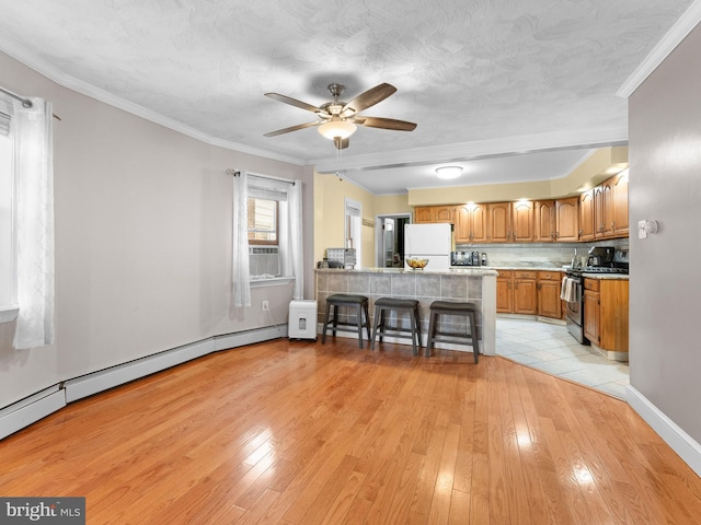 kitchen featuring stainless steel gas stove, white refrigerator, a kitchen breakfast bar, kitchen peninsula, and light hardwood / wood-style floors