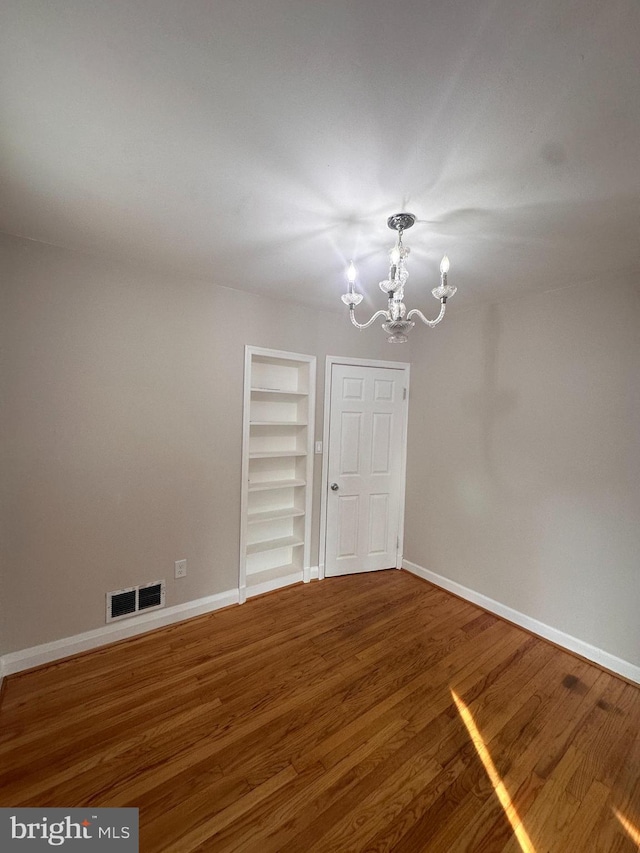 empty room featuring an inviting chandelier, built in shelves, and hardwood / wood-style flooring