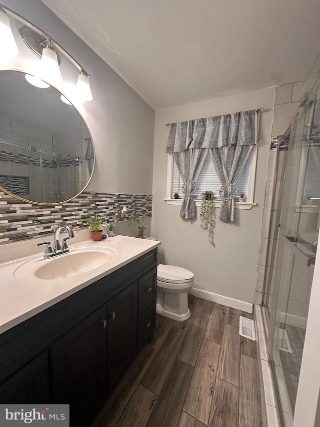 bathroom with toilet, a shower with shower door, vanity, hardwood / wood-style flooring, and decorative backsplash