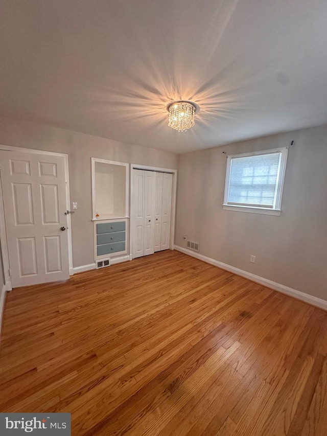 unfurnished bedroom with an inviting chandelier, light hardwood / wood-style floors, and a closet