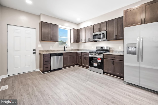 kitchen featuring light stone counters, stainless steel appliances, sink, and light hardwood / wood-style flooring