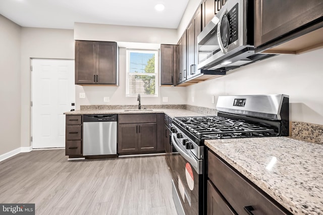 kitchen featuring sink, stainless steel appliances, light stone countertops, dark brown cabinets, and light hardwood / wood-style flooring