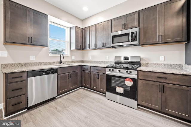 kitchen with light stone counters, sink, dark brown cabinets, and appliances with stainless steel finishes