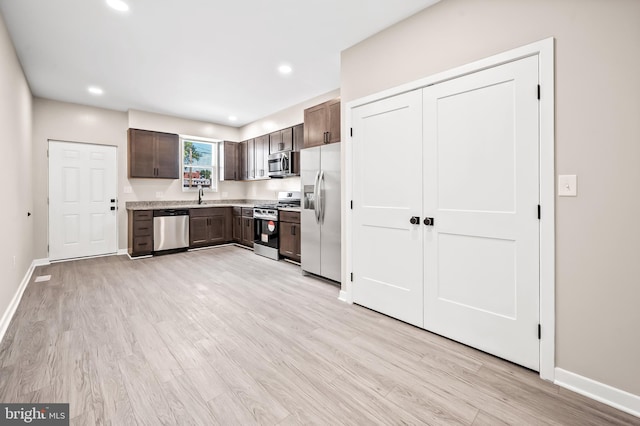 kitchen featuring dark brown cabinetry, sink, light stone counters, stainless steel appliances, and light hardwood / wood-style floors