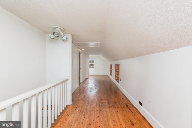 hall featuring vaulted ceiling, built in features, a textured ceiling, and light hardwood / wood-style floors