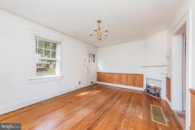 unfurnished living room with an inviting chandelier and hardwood / wood-style flooring