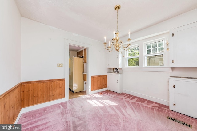 unfurnished dining area with wooden walls, a chandelier, and light carpet