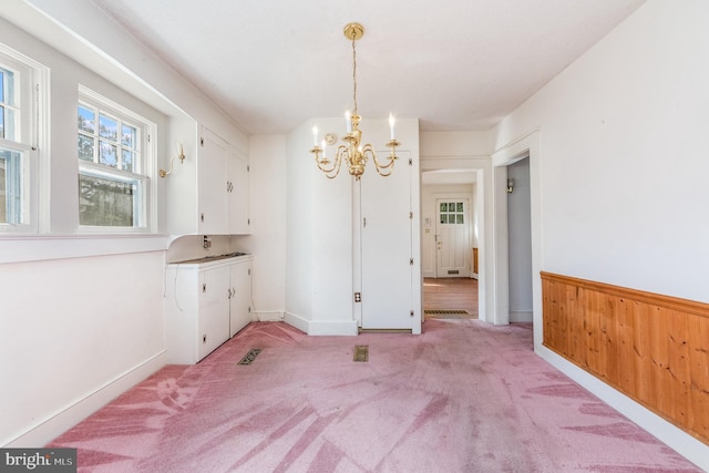 unfurnished dining area featuring light carpet, a chandelier, and wood walls