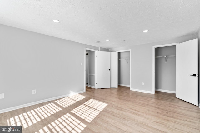 unfurnished bedroom featuring two closets, a textured ceiling, and light wood-type flooring