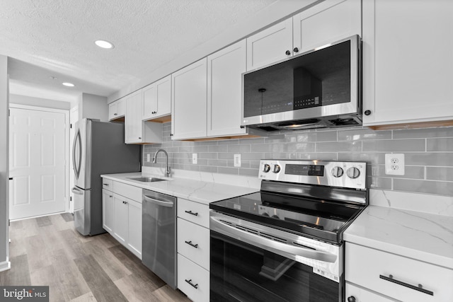 kitchen featuring sink, light hardwood / wood-style flooring, stainless steel appliances, light stone countertops, and white cabinets