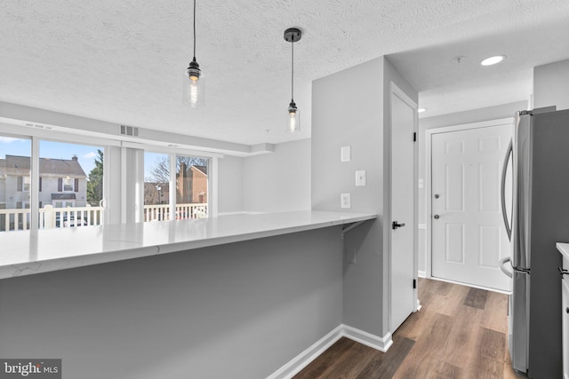 kitchen with dark hardwood / wood-style floors, stainless steel refrigerator, hanging light fixtures, light stone counters, and kitchen peninsula