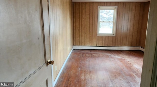 empty room featuring hardwood / wood-style flooring, wooden walls, and baseboard heating