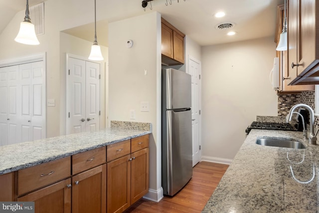 kitchen featuring visible vents, brown cabinets, a sink, and freestanding refrigerator