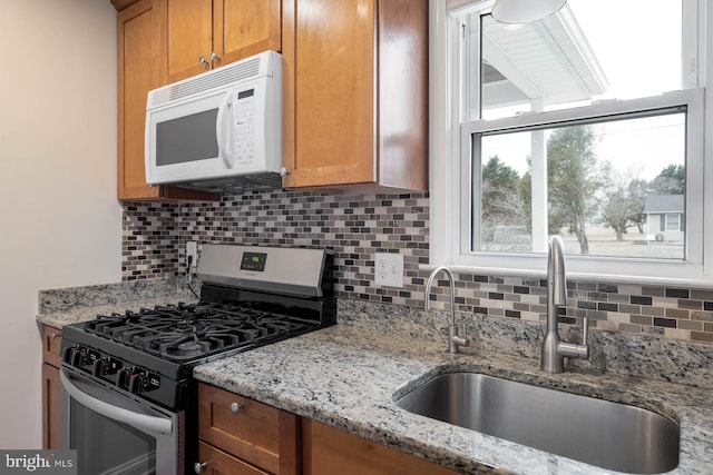 kitchen with decorative backsplash, white microwave, light stone counters, stainless steel gas range, and a sink