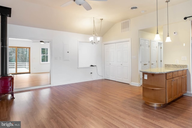 kitchen featuring visible vents, lofted ceiling, wood finished floors, a wood stove, and ceiling fan with notable chandelier