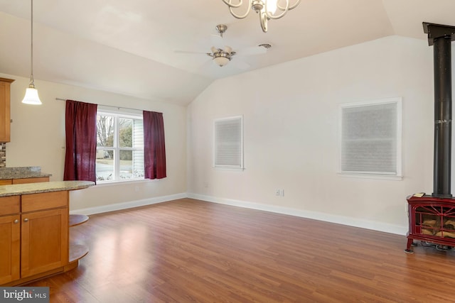 unfurnished living room featuring a ceiling fan, baseboards, vaulted ceiling, light wood-style floors, and a wood stove