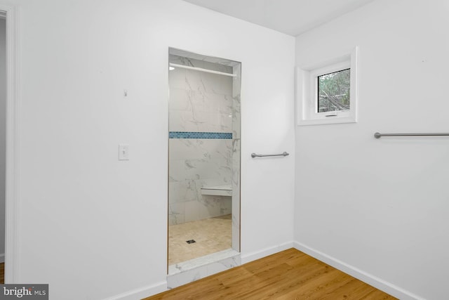 full bath with a marble finish shower, baseboards, and wood finished floors