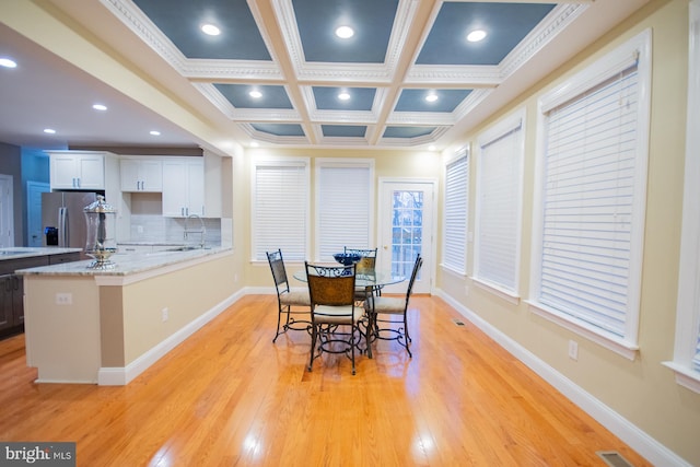 dining space featuring light wood-style flooring, baseboards, coffered ceiling, and beamed ceiling