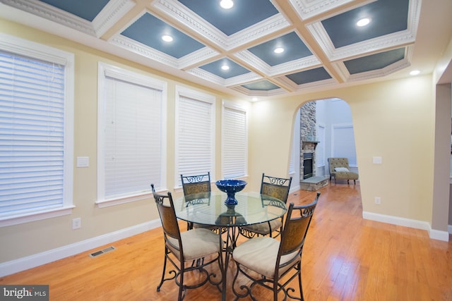 dining space with arched walkways, a fireplace, visible vents, light wood-type flooring, and baseboards