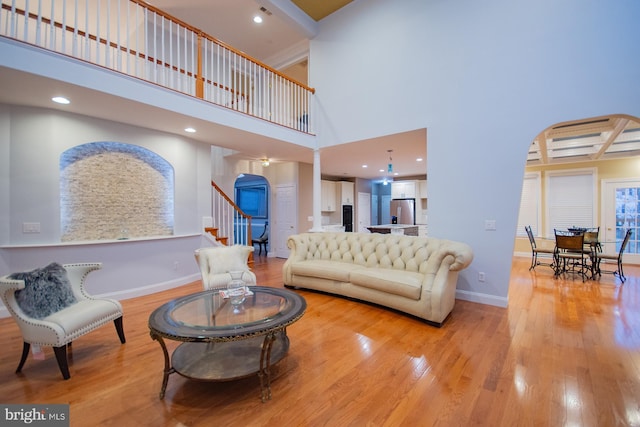 living area with light wood finished floors, baseboards, arched walkways, a high ceiling, and stairs