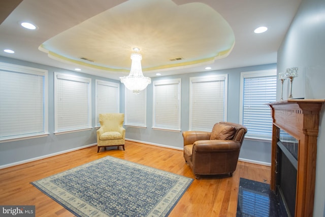 living area with a tray ceiling, wood finished floors, and visible vents