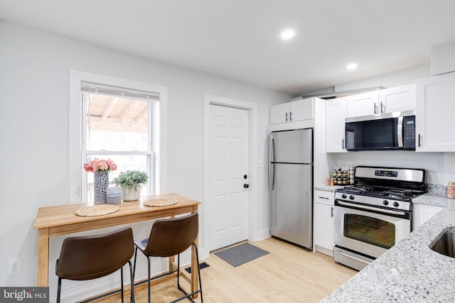 kitchen featuring stainless steel appliances, white cabinetry, light wood-type flooring, and light stone counters