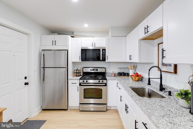 kitchen with sink, white cabinets, stainless steel appliances, light stone countertops, and light hardwood / wood-style flooring