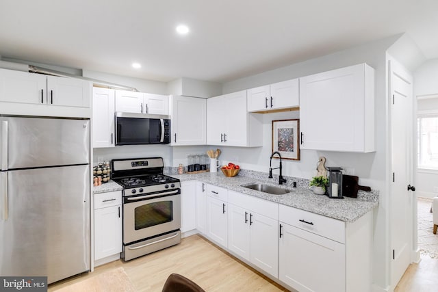 kitchen with sink, light hardwood / wood-style flooring, appliances with stainless steel finishes, light stone countertops, and white cabinets