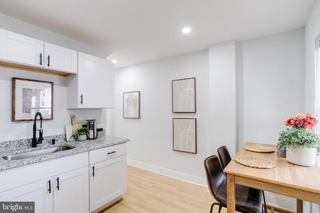 kitchen with white cabinetry, sink, light stone counters, and light wood-type flooring