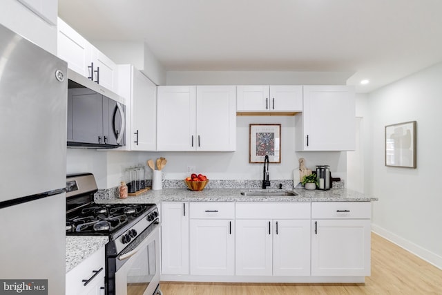 kitchen with sink, appliances with stainless steel finishes, light stone counters, light hardwood / wood-style floors, and white cabinets