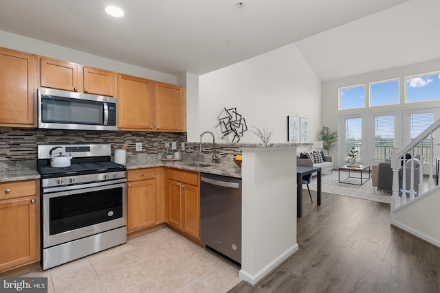 kitchen with appliances with stainless steel finishes, tasteful backsplash, sink, light stone counters, and kitchen peninsula