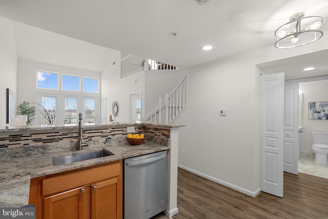 kitchen with sink, backsplash, dark hardwood / wood-style floors, light stone countertops, and stainless steel dishwasher