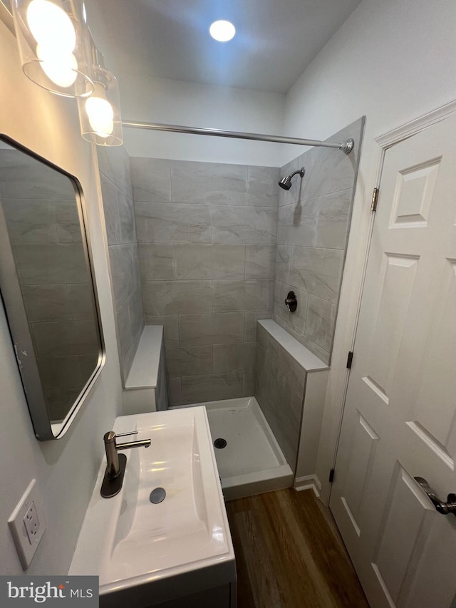 bathroom with wood-type flooring, tiled shower, and vanity