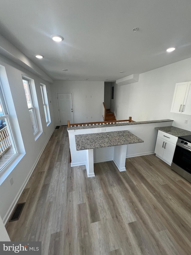 kitchen featuring a breakfast bar, hardwood / wood-style floors, white cabinetry, electric range, and kitchen peninsula