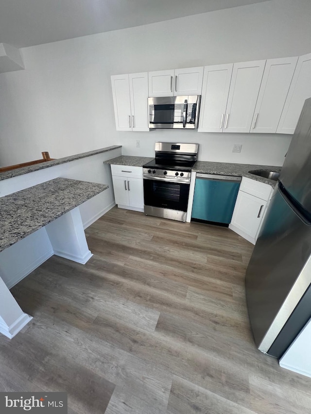 kitchen with sink, appliances with stainless steel finishes, dark stone counters, light hardwood / wood-style floors, and white cabinets