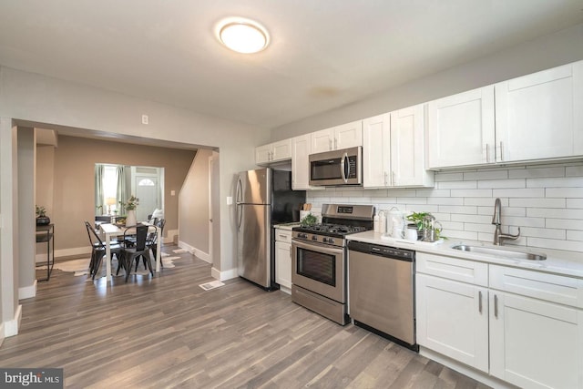 kitchen with hardwood / wood-style floors, sink, white cabinets, decorative backsplash, and stainless steel appliances