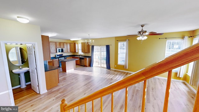 kitchen featuring ceiling fan with notable chandelier, pendant lighting, sink, light hardwood / wood-style floors, and stainless steel appliances