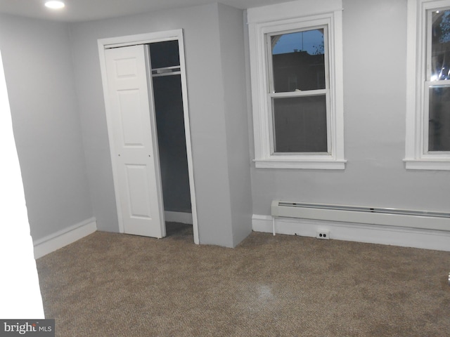 unfurnished bedroom featuring a baseboard heating unit, carpet floors, and a closet