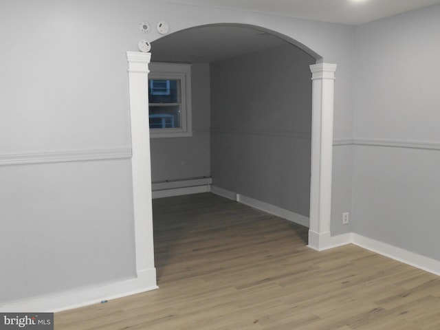 corridor with baseboard heating, hardwood / wood-style floors, and decorative columns