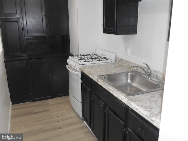 kitchen featuring light stone countertops, sink, gas range gas stove, and light hardwood / wood-style flooring