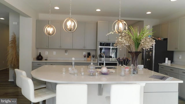 kitchen featuring sink, dark wood-type flooring, gray cabinets, a center island with sink, and stainless steel double oven