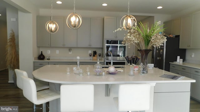 kitchen with dark hardwood / wood-style floors, sink, gray cabinetry, stainless steel double oven, and a center island with sink